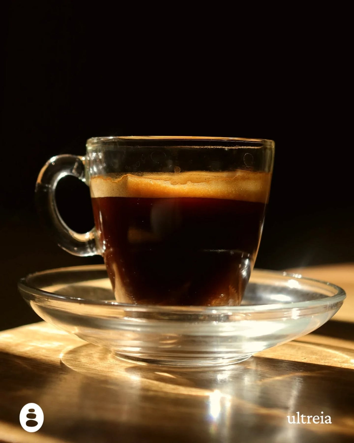 Un espresso en taza de vidrio, con luz de ventana sobre la mesa.